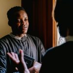 Two seminarians discussing religious teachings with a Bible in hand, bathed in natural light.